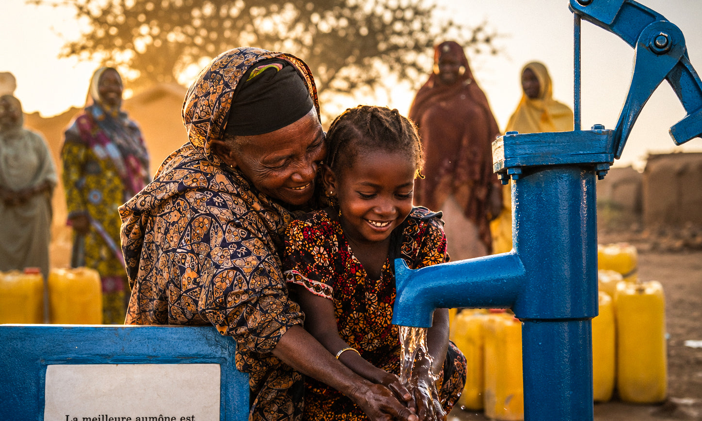 Une grand-mère aide une enfant à boire l'eau d'une pompe Sanabil.